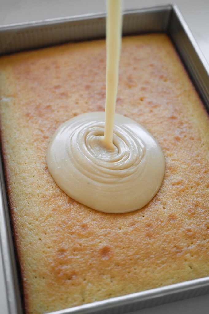 A smooth caramel frosting being poured onto a baked cake.