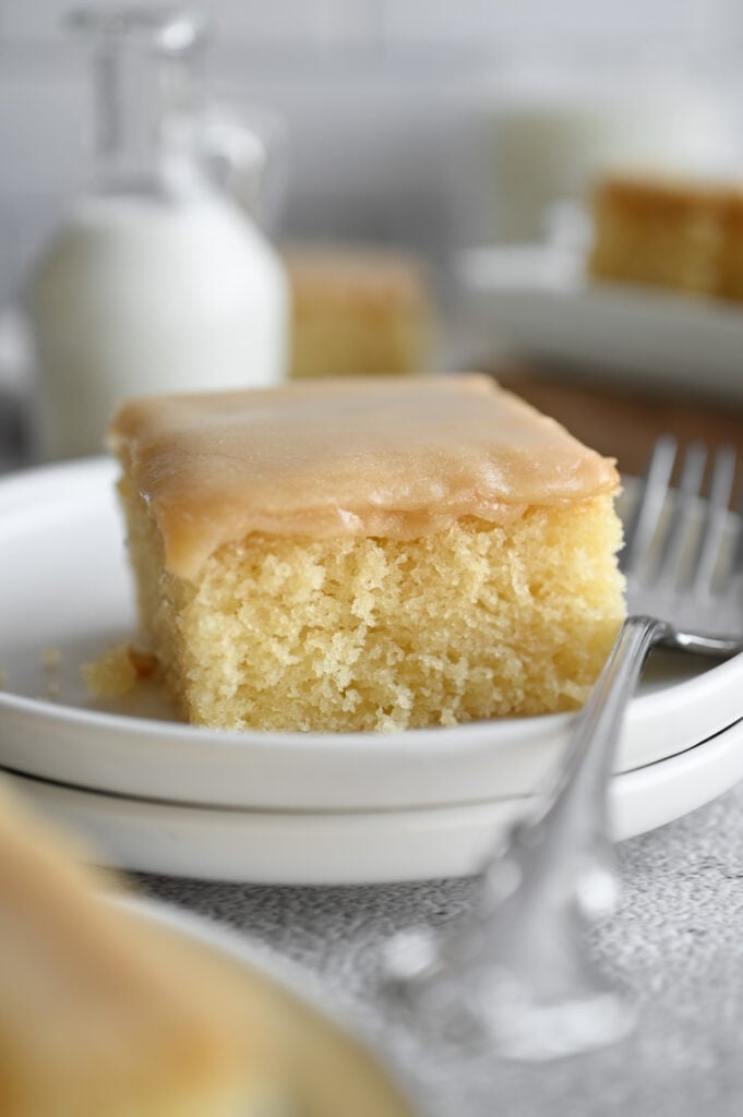 A square slice of buttermilk cake on a white plate with a silver fork.
