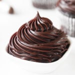 Glossy chocolate frosting piped with a star piping tip into a small white ramekin.