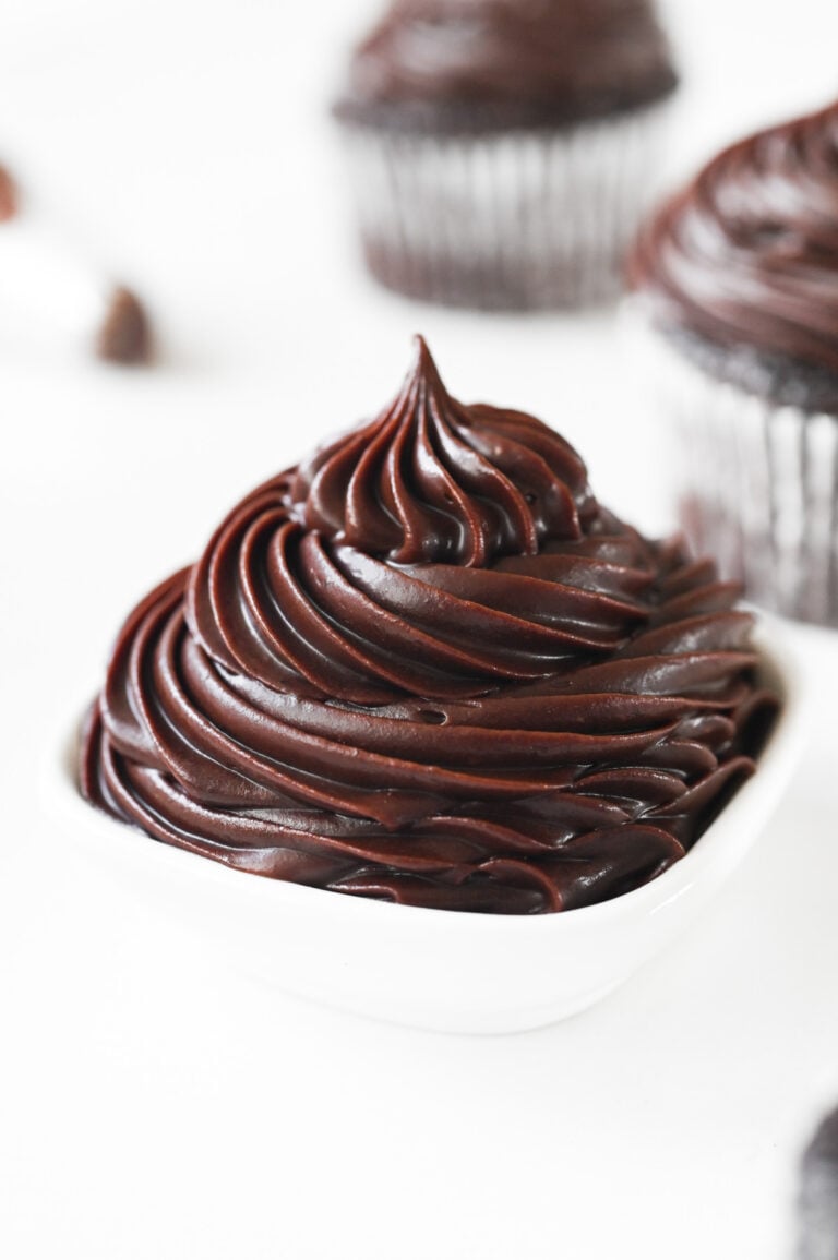 Glossy chocolate frosting piped with a star piping tip into a small white ramekin.