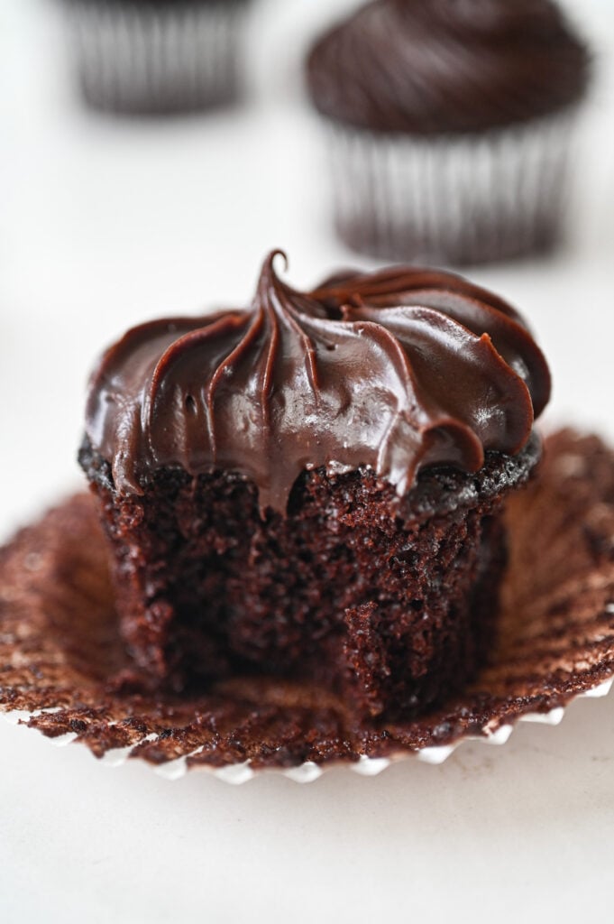 A chocolate cupcake with chocolate frosting; liner is removed and a bite is out of the cupcake.