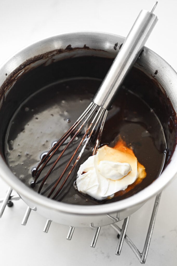 A saucepan with a runny chocolate mixture, sour cream, and vanilla extract.