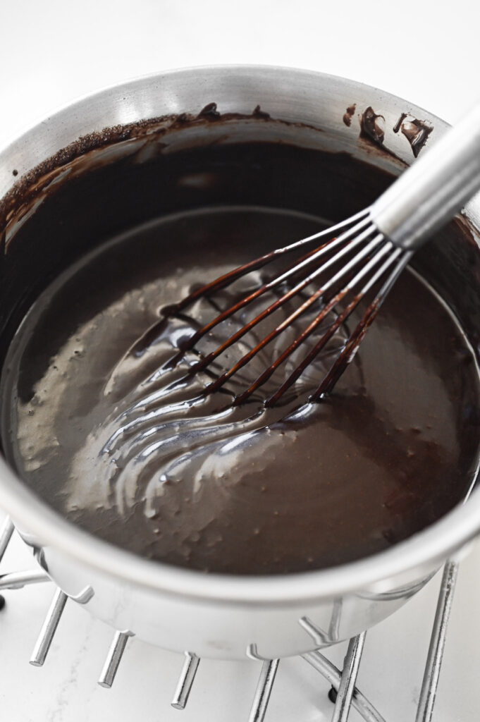 A whisk mixing a chocolate frosting.