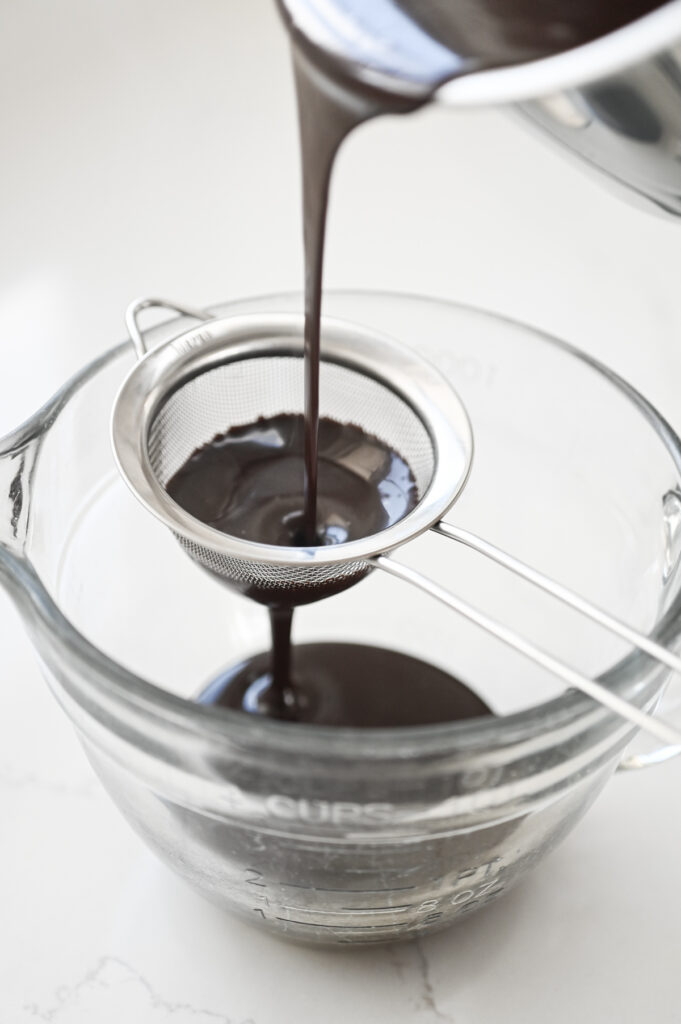 Chocolate sauce mixture being poured into a fine sieve.