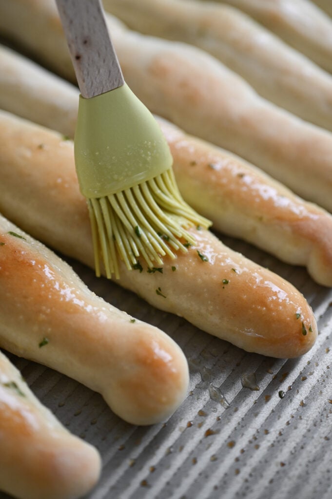 A pastry brush brushing melted butter on a baked breadstick.