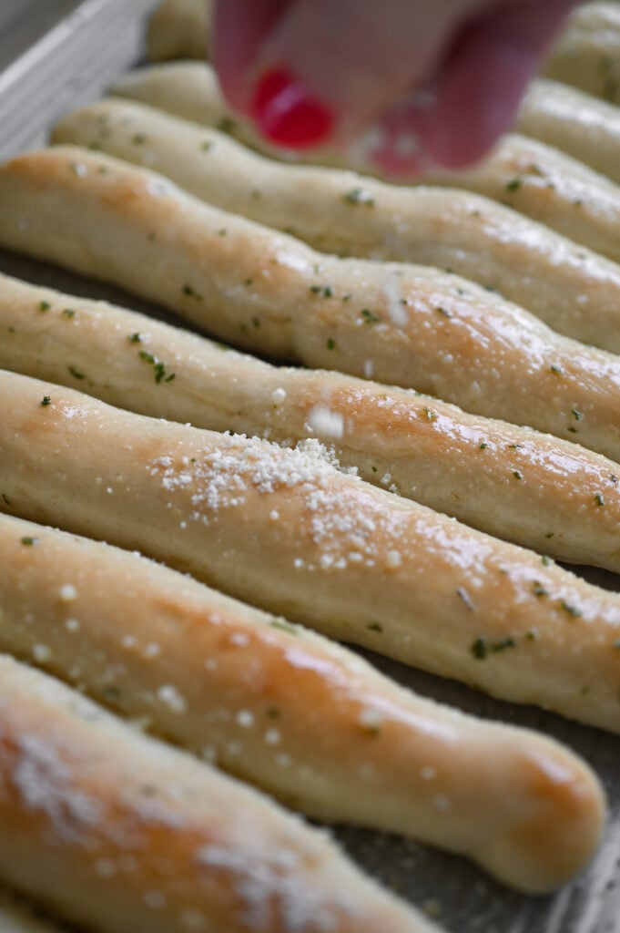 A hand sprinkling parmesan cheese on hot breadsticks.