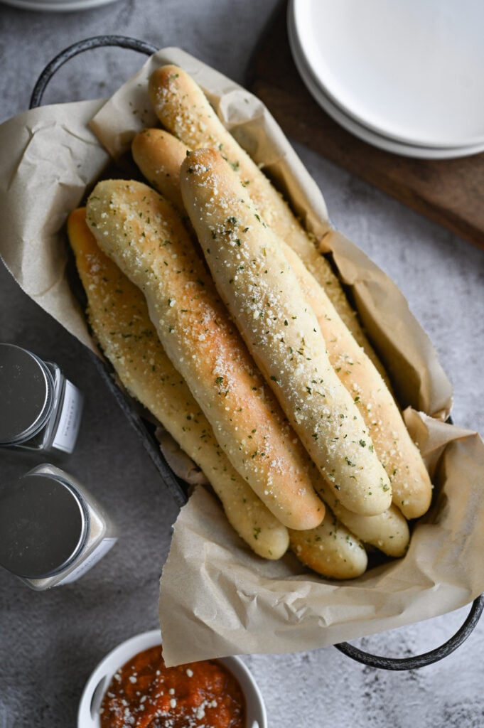 A basket of breadsticks with marinara on the side.