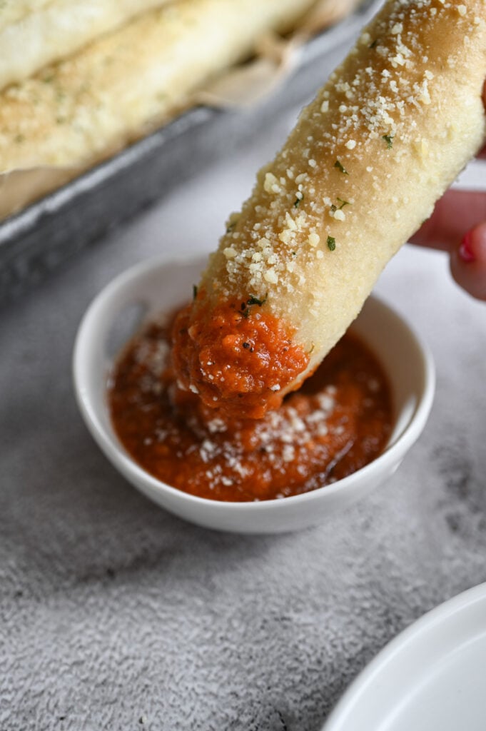 A breadstick being dipped in pizza sauce.