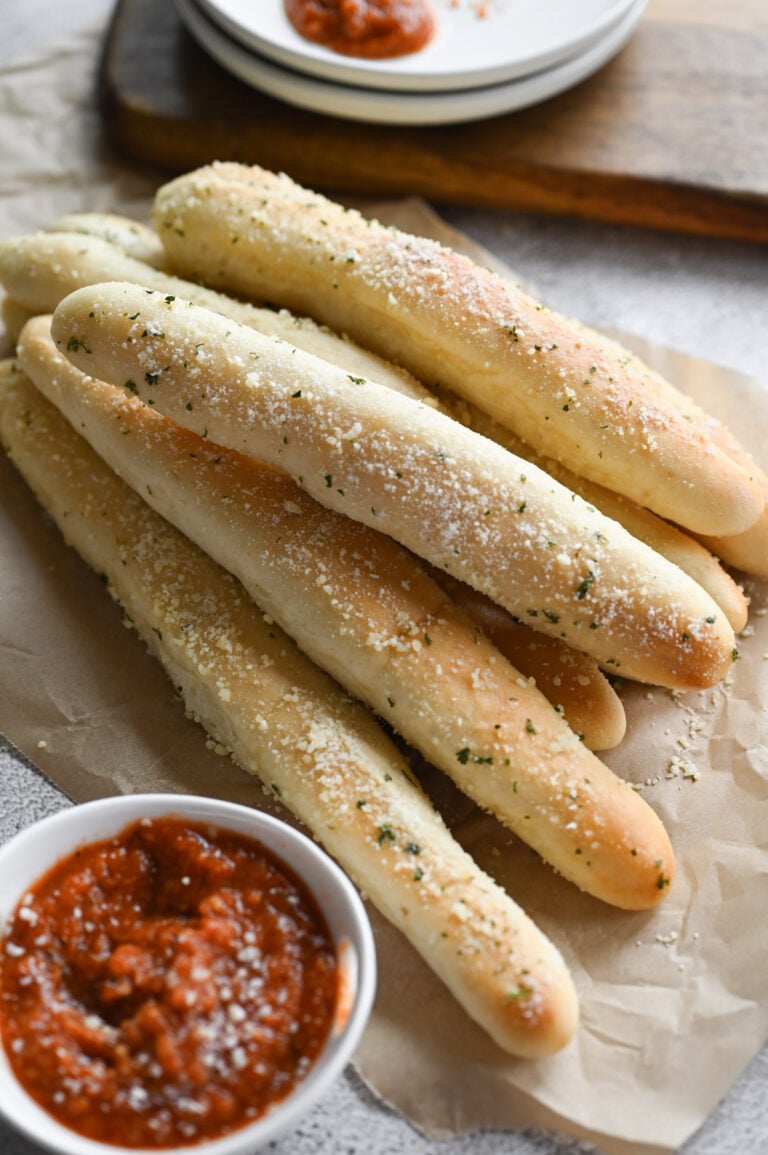 Several breadsticks on a piece of parchment paper with a small dish of marinara sauce next to it.