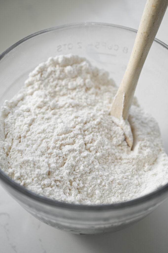 A rubber spatula stirring together some dry white ingredients in a bowl