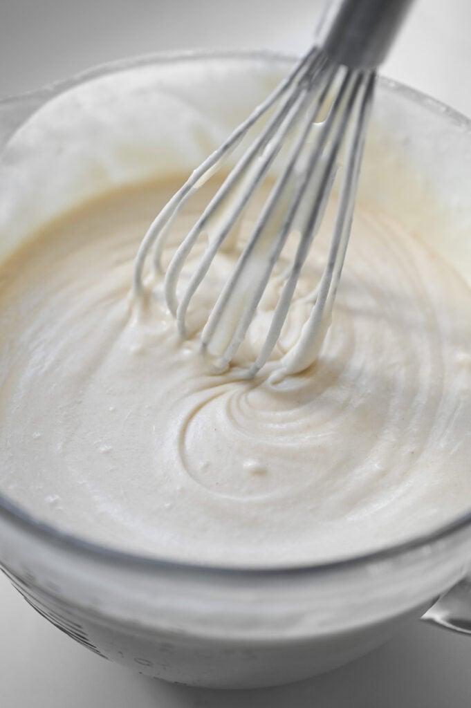 A whisk stirring a white cake batter.