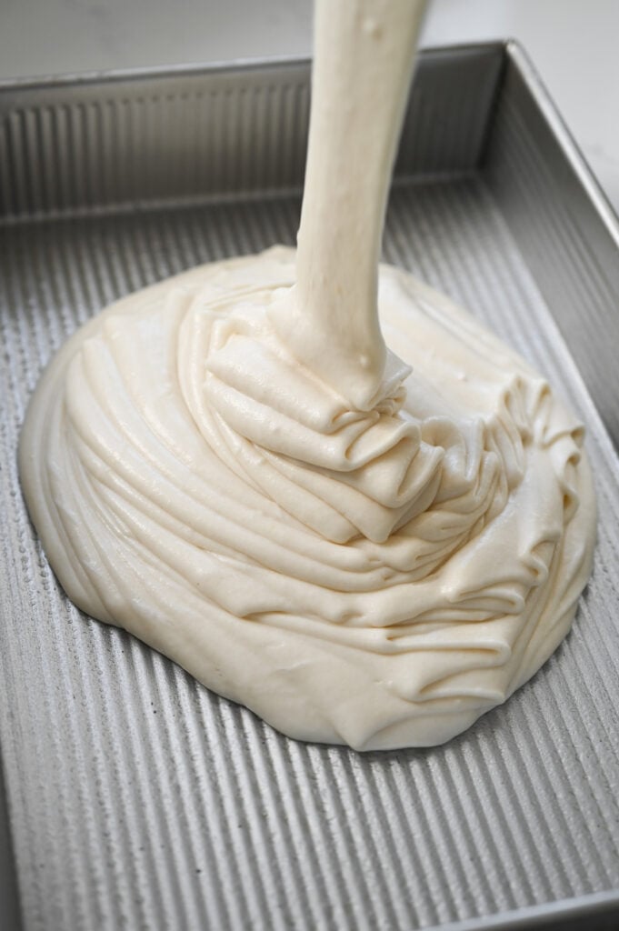 White cake batter being poured into a 9x13-inch pan.