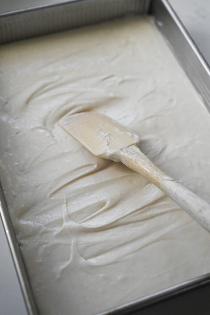 A rubber spatula spreading cake batter into a 9x13-inch pan.
