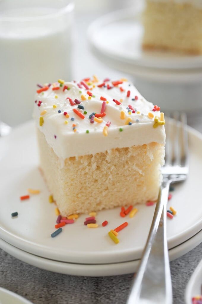 A square of white cake with frosting and sprinkles on top.