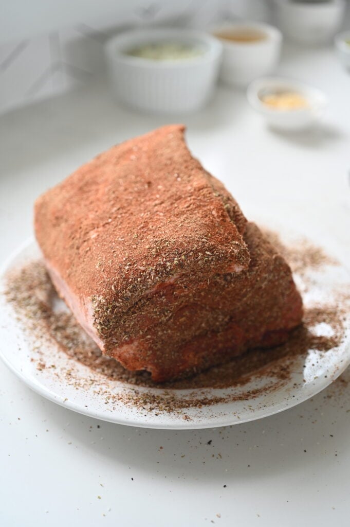 A pork roast on a white plate with a pork rub all over it.