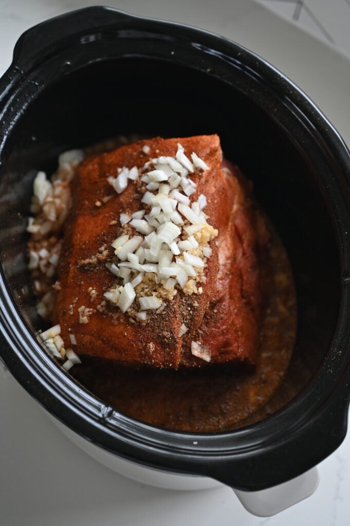A pork roast in a slow cooker with veggies and juices.