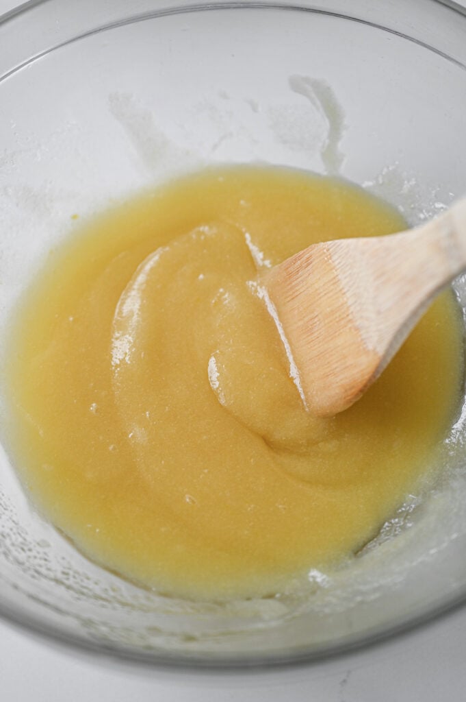 A light yellow mixture being stirred by a wooden spoon.