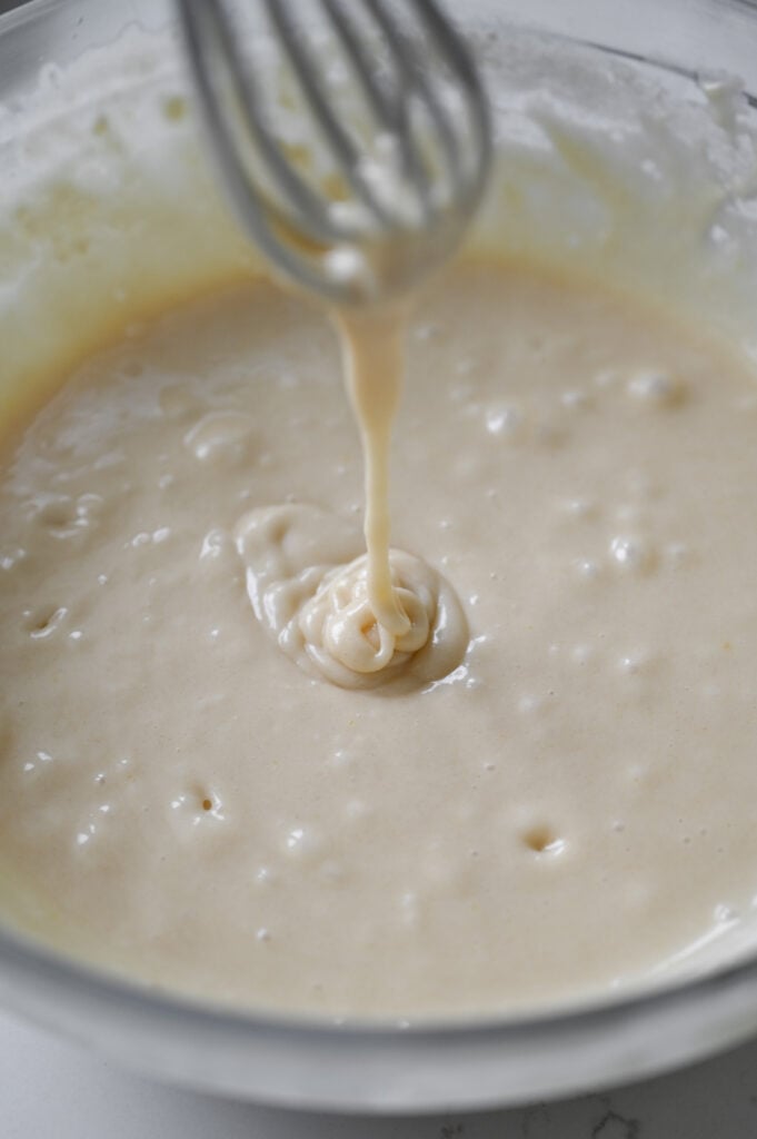 A bowl of batter; a whisk is lifted up as batter streams beneath.
