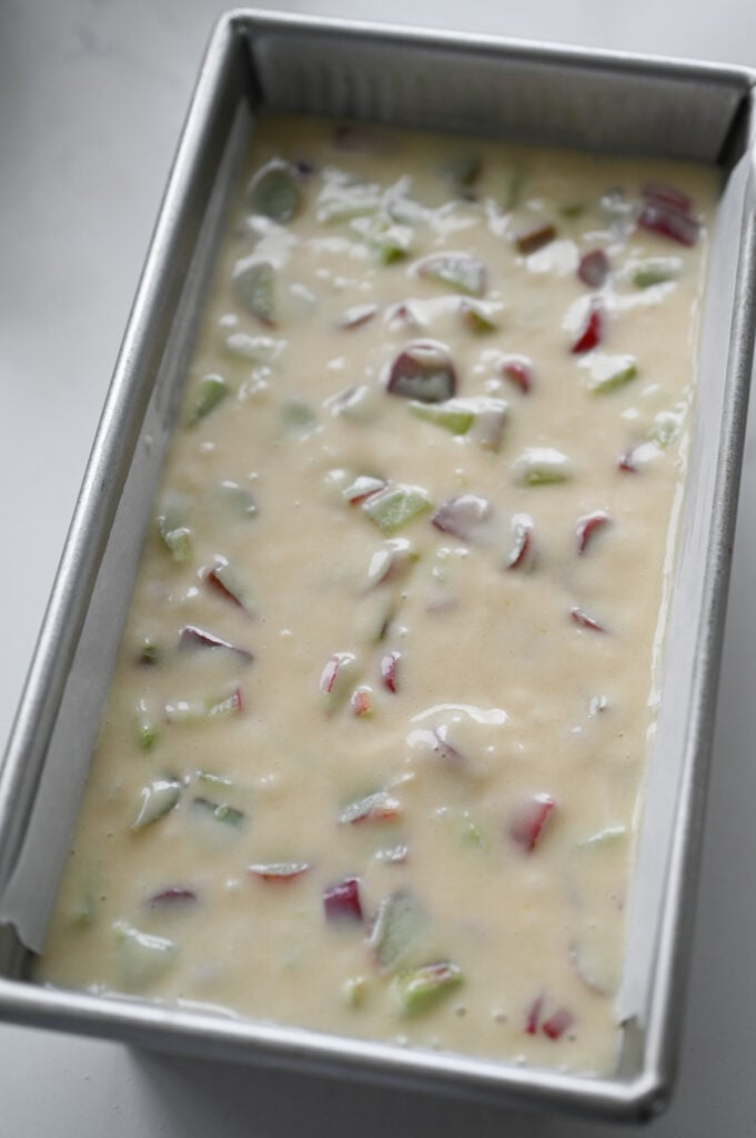 A loaf pan with rhubarb bread batter spread in it.