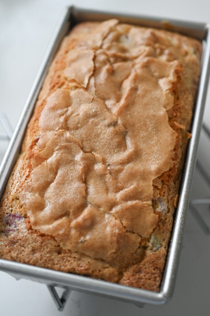 A baked loaf of quick bread in a loaf pan on a cooling rack.