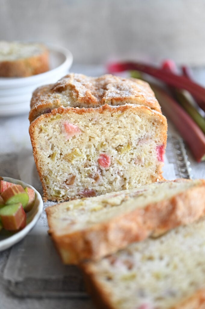 A loaf of rhubarb bread on a wire rack with a few slices.