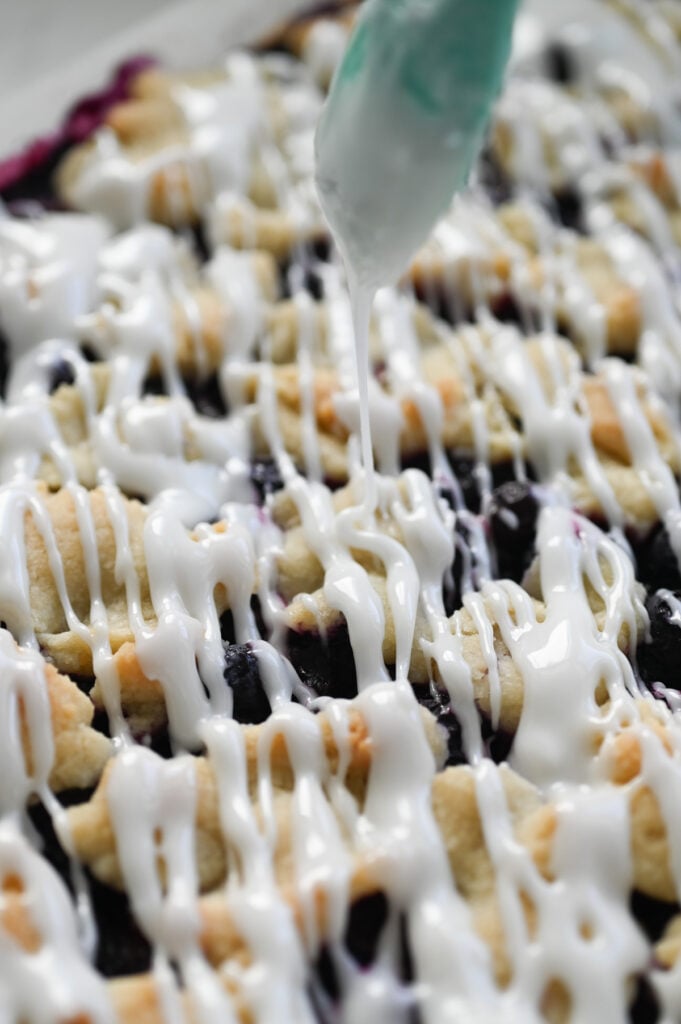 Icing being drizzled over a pan of blueberry crumble bars.