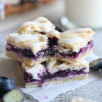 Two blueberry crumble bars stacked on one another; the top one has a bite out of it.