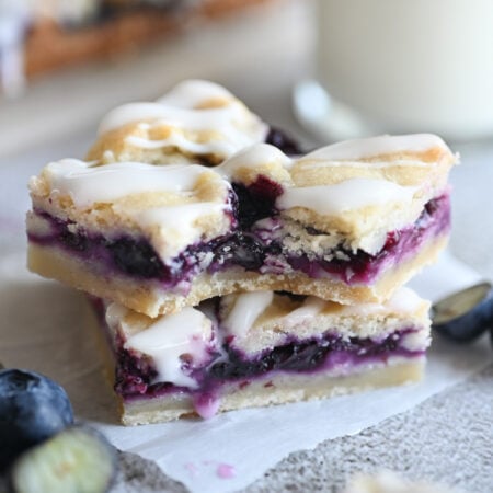 Two blueberry crumble bars stacked on one another; the top one has a bite out of it.