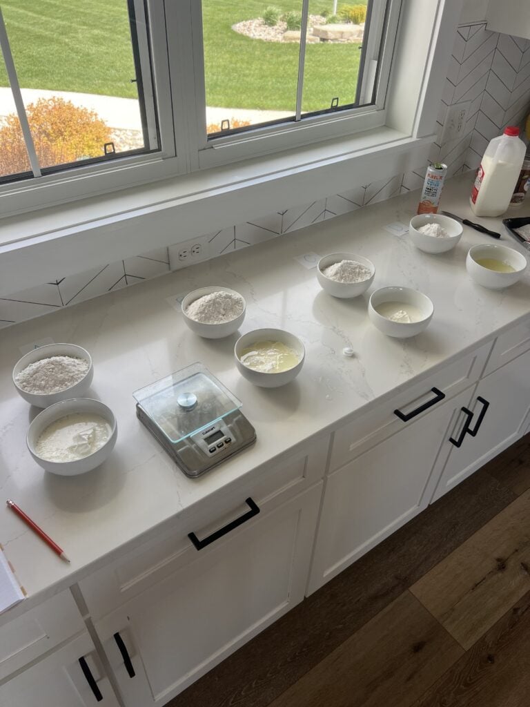 A kitchen with recipe testing going on; lots of bowls on a white surface and a kitchen scale.