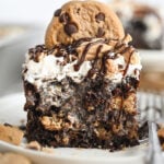 A piece of chocolate chip cookie poke cake on a white plate with a small cookie on top for garnish.