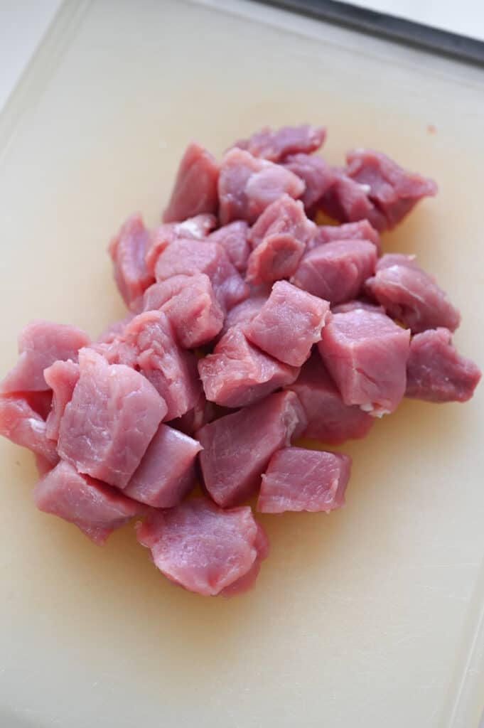Pork tenderloin cut into 1 inch cubes on a clear cutting board.