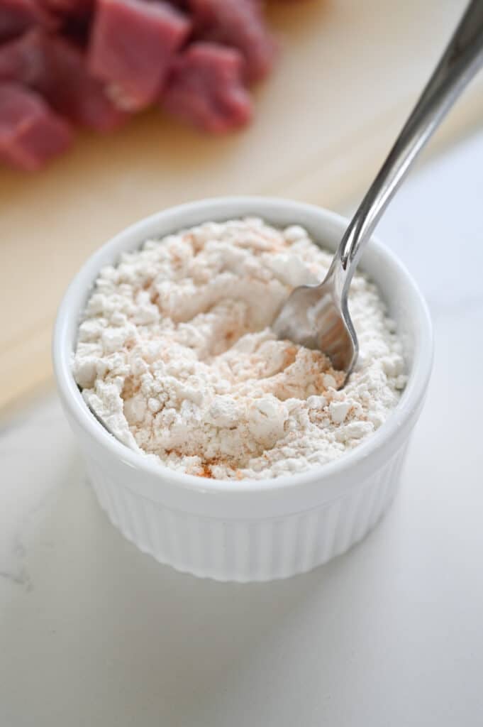 The breading mixture (cornstarch and flour) in a small white ramekin with a spoon.