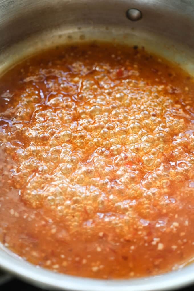 A red-orange sauce boiling in a saute pan.