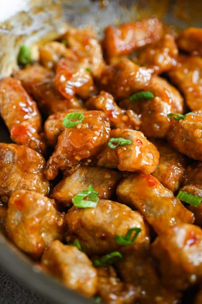 Close-up of a pan of sticky pork with sliced green onions on top.