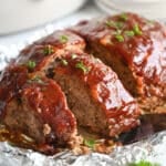Meatloaf in front of a slow cooker; the meatloaf is sliced and a spatula is grabbing a slice.