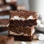 Two marshmallow crunch brownies on a gray stone background with a glass of milk behind it.