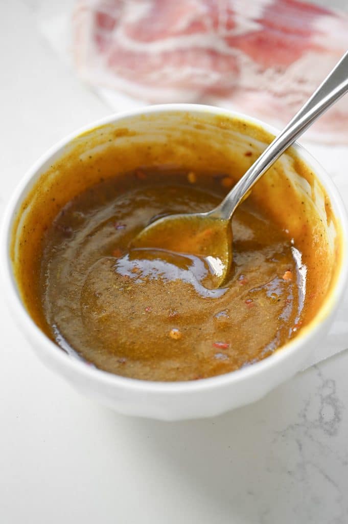 A yellowish brown sauce in a white bowl with a spoon.