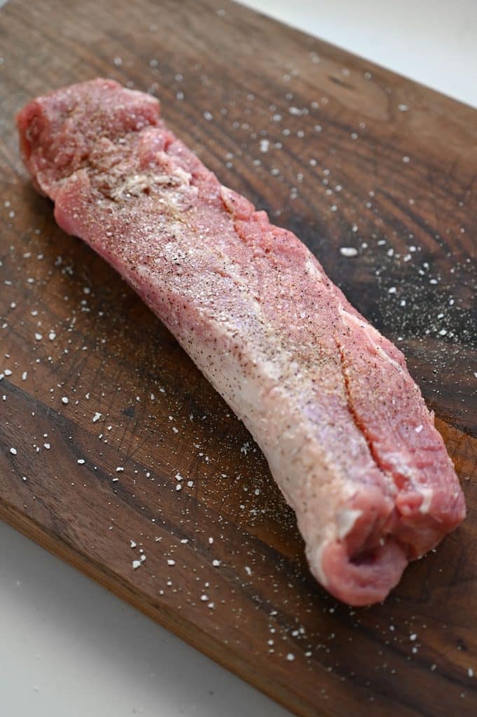 A pork tenderloin seasoned on a wooden cutting board.