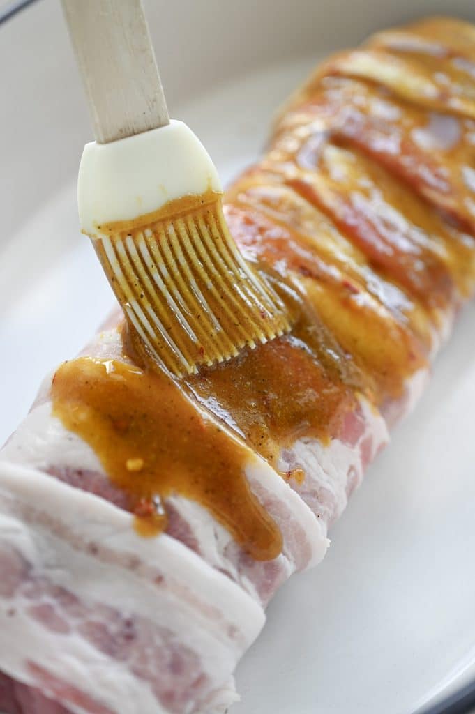 Brushing a glaze on a bacon wrapped pork tenderloin.