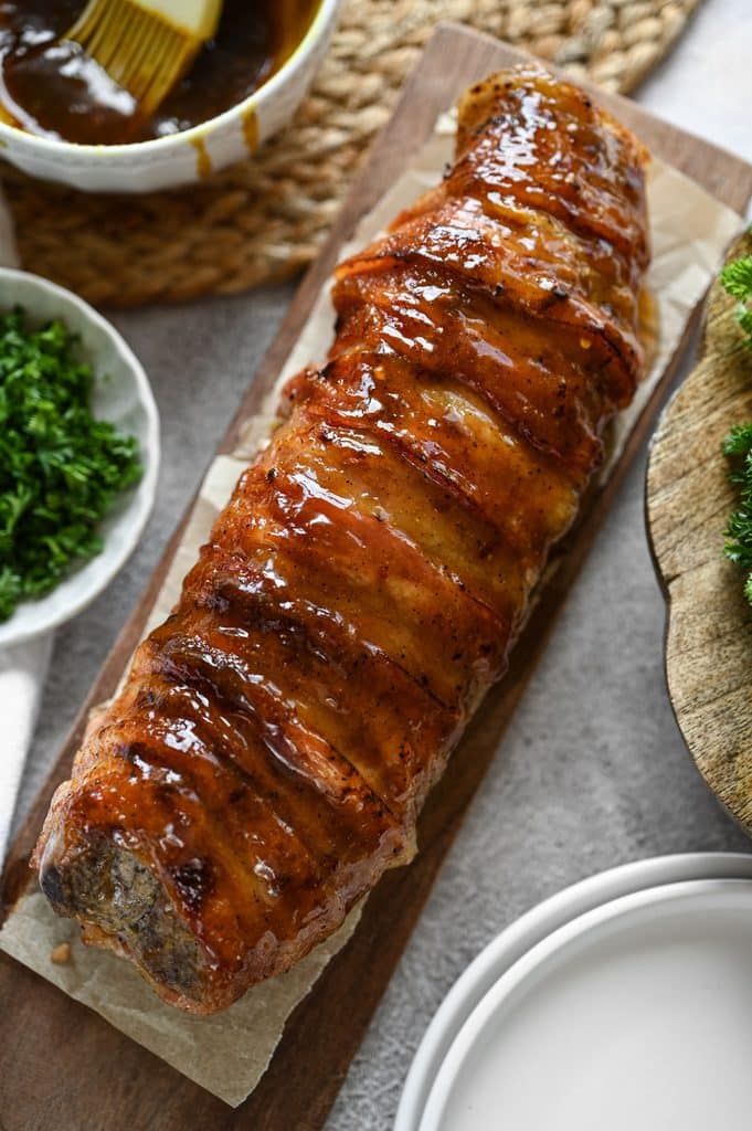 A bacon wrapped pork tenderloin with a glossy glaze on it.