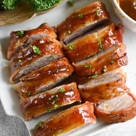 Bacon Wrapped Pork Tenderloin on a white platter.
