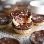 Two Twix Cookie Cups stacked on eachother; the one on top has a bite out of it and the caramel is dripping out.