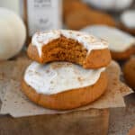 Two soft pumpkin cookies frosted with cream cheese frosting. The top cookie has a bite out of it.